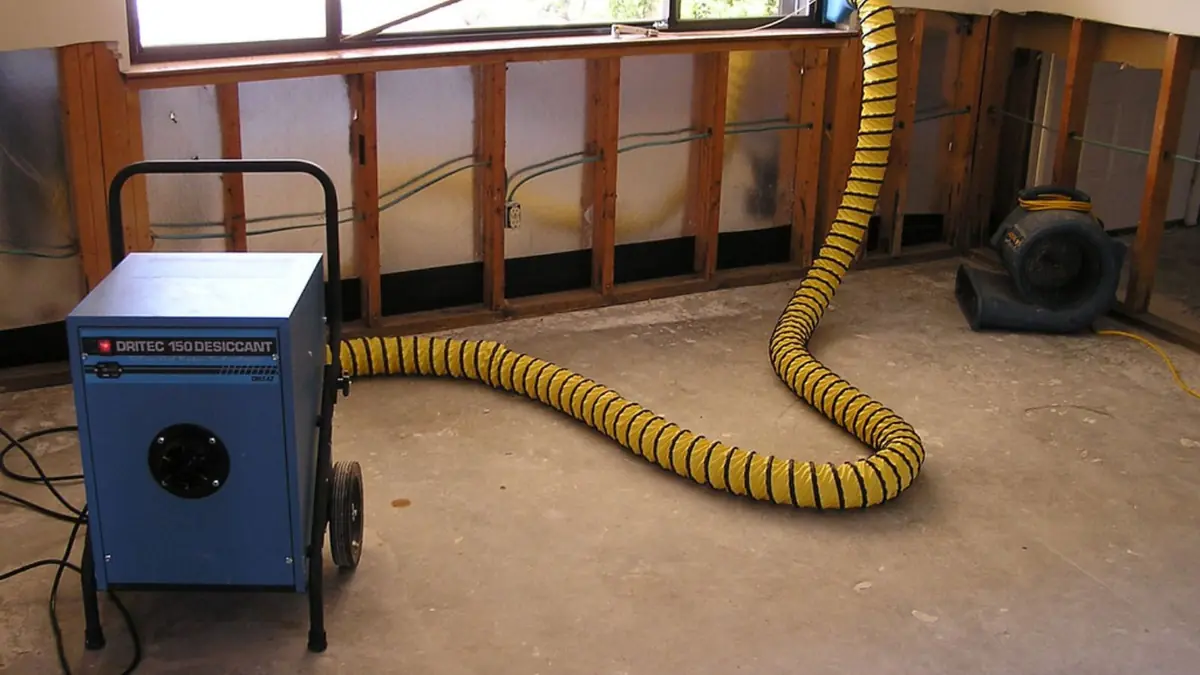 Dehumidifier with a yellow duct drying an opened wall cavity